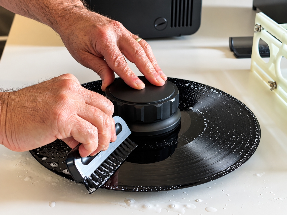 Rick’s hands scrubbing a wet, soapy record with a brush while a label protector covers the center.
